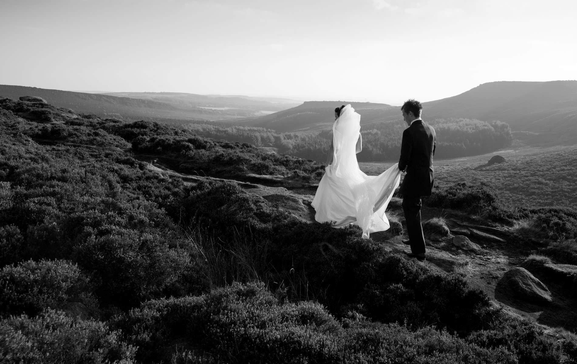 Wedding photographer Ashford snapping couple walking up hill rural groom holding train black and white